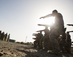 New Zealand Army soldiers perform a haka in the right of image to a group of people at Camp Taji