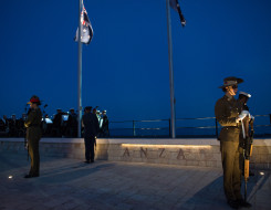 NZDf personnel stand in a catafalque guard at the Anzac Commemorative Site in Gallipoli. Thee New Zealand and Australian flags are flying from flag poles and it is dark as the ceremony is at dawn.