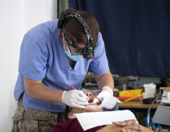 An NZDF dentist working on a patients mouth using a head torch. 