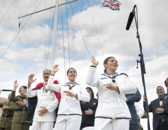 NZDF personnel perform and sing a waiata near a flag mask. Three Royal New Zealand Navy sailors are in the foreground. 