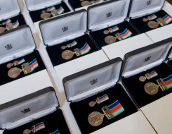 Many boxes of New Zealand Defence Service Medals. In each box is the medal, a bronze medal with an antique finish suspended from a dark blue, red, light blue and light green ribbon. 