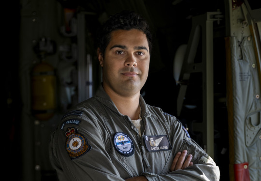 An aviator stands armed crossed looking at the camera in a flying suit.