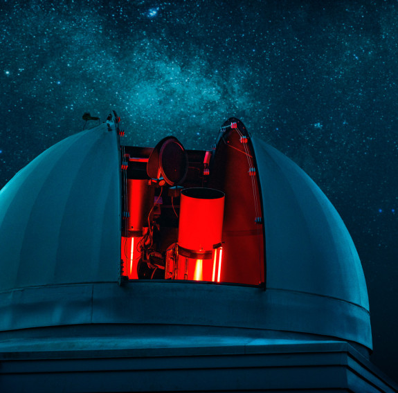 The Defence Science Technology telescope sits under the stars. The outer dome opens across the centre to reveal a glowing red telescope.